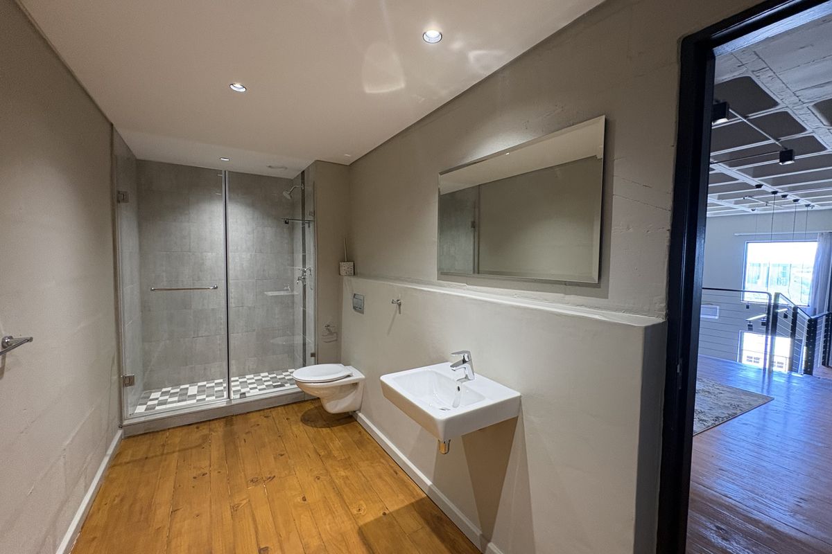 Modern bathroom featuring a glass-enclosed shower, wall-mounted toilet, and a sleek wall-hung basin with a large mirror.