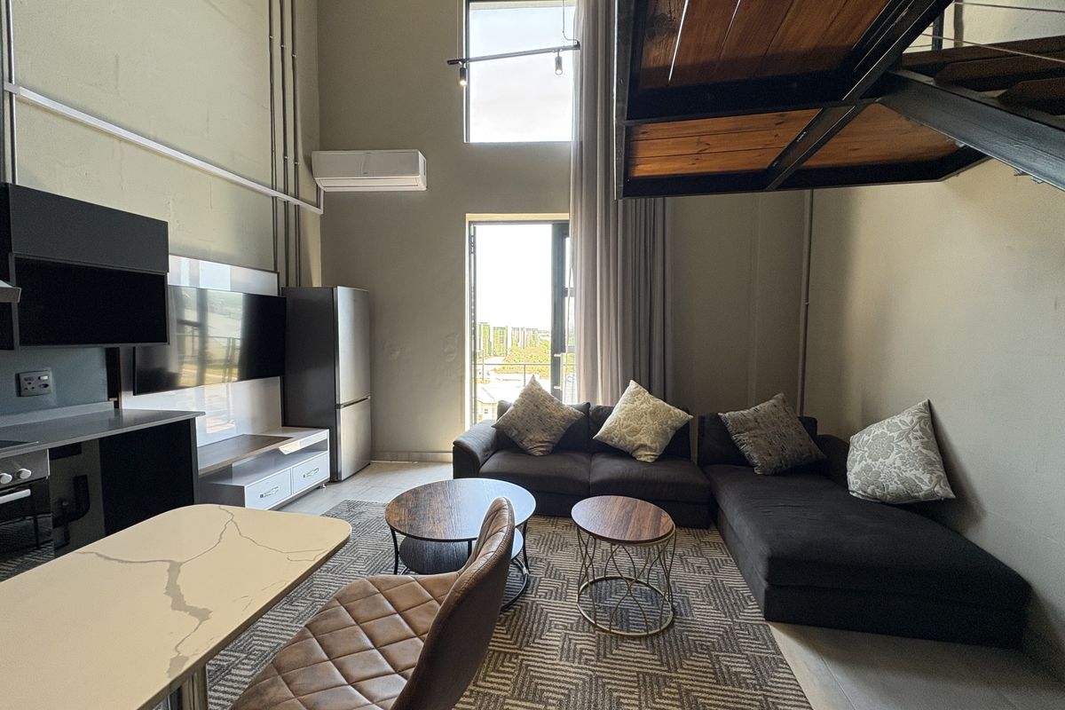 Open-plan living area featuring double-volume ceilings, industrial-style staircase, large windows, and integrated kitchen cabinetry with modern finishes.