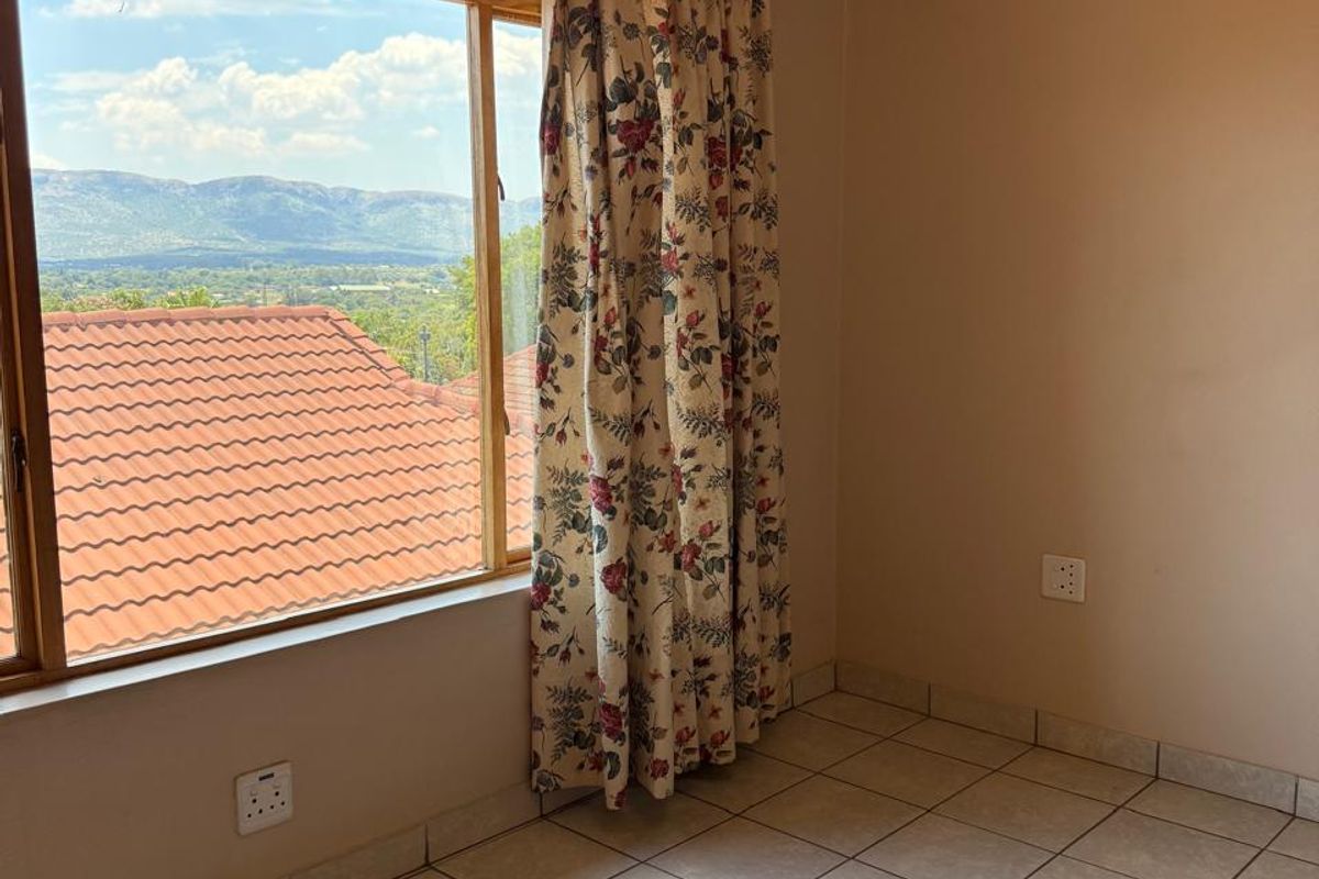 A bright, empty bedroom featuring tiled flooring, neutral walls, and a large window offering scenic mountain views.