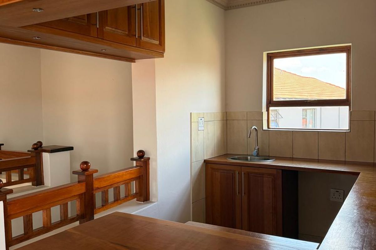A functional kitchen area featuring wooden cabinetry, a built-in breakfast bar, and a stainless steel sink with tiled splashback.