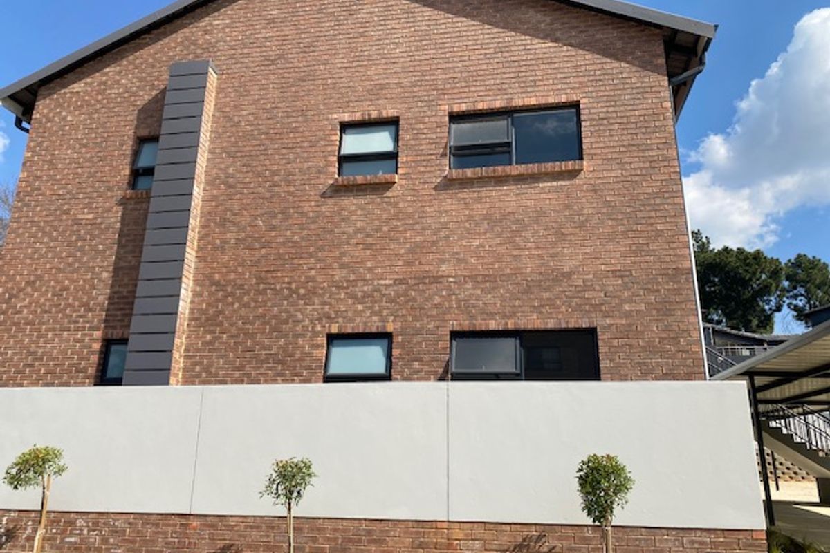 A view of the exterior brick facade of the apartment building, featuring modern window frames and a clean, rendered boundary wall.