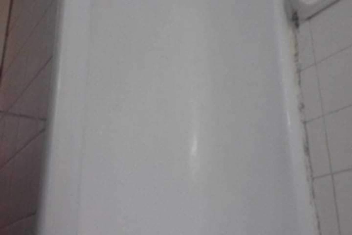 A close-up view of a standard bathtub featuring white ceramic wall tiles and a built-in soap dish.