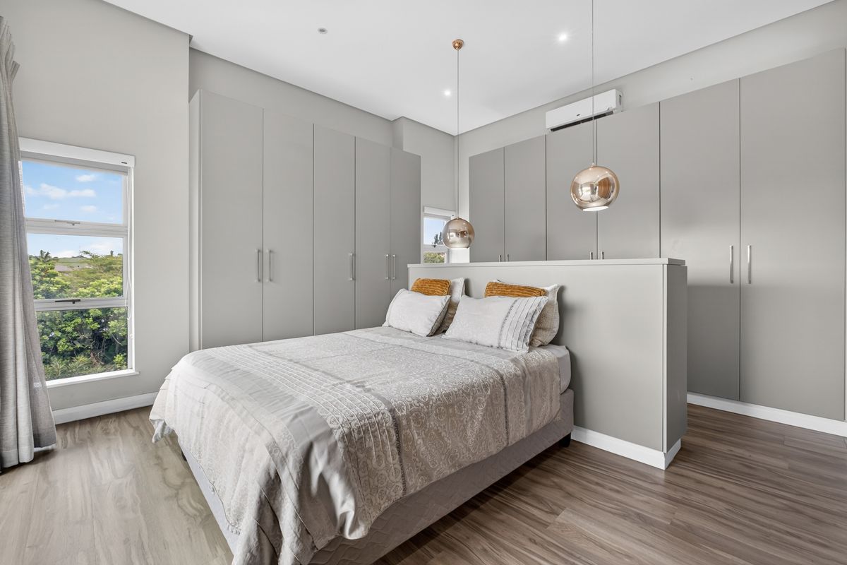 Modern bedroom featuring extensive built-in cabinetry, wood-look flooring, split-system air conditioning, and a central partition wall behind the bed.
