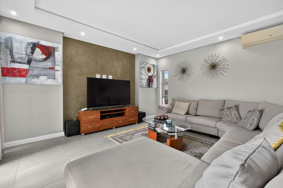 A modern living room featuring recessed ceiling lighting, tiled flooring, and a feature wall, providing a comfortable and well-maintained space for relaxation.