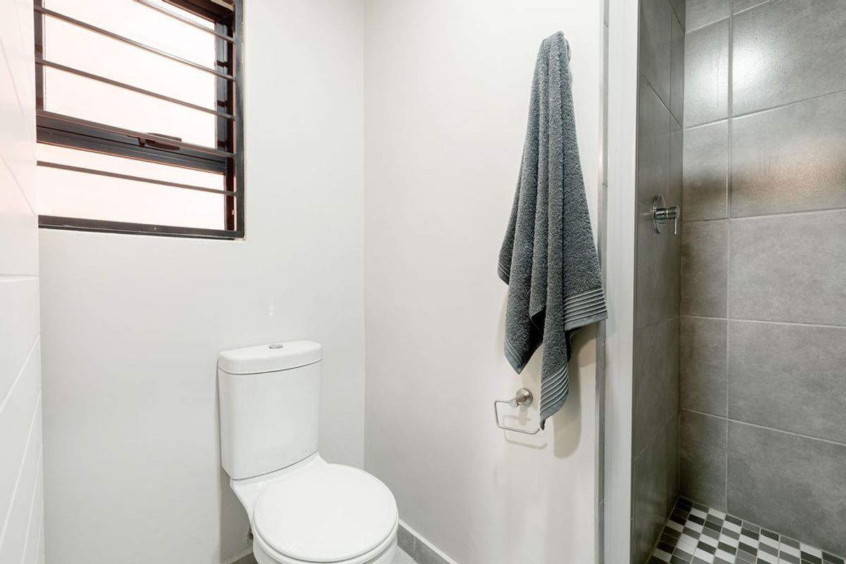 A modern bathroom featuring a walk-in shower with grey tiling, a white toilet, and a window with security bars.