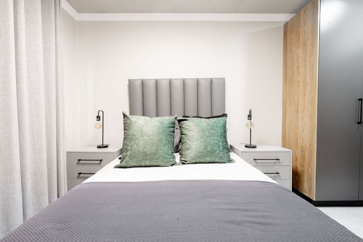 A modern, well-maintained bedroom featuring a built-in wardrobe with wood-grain and dark grey finishes, neutral wall tones, and a contemporary upholstered headboard.