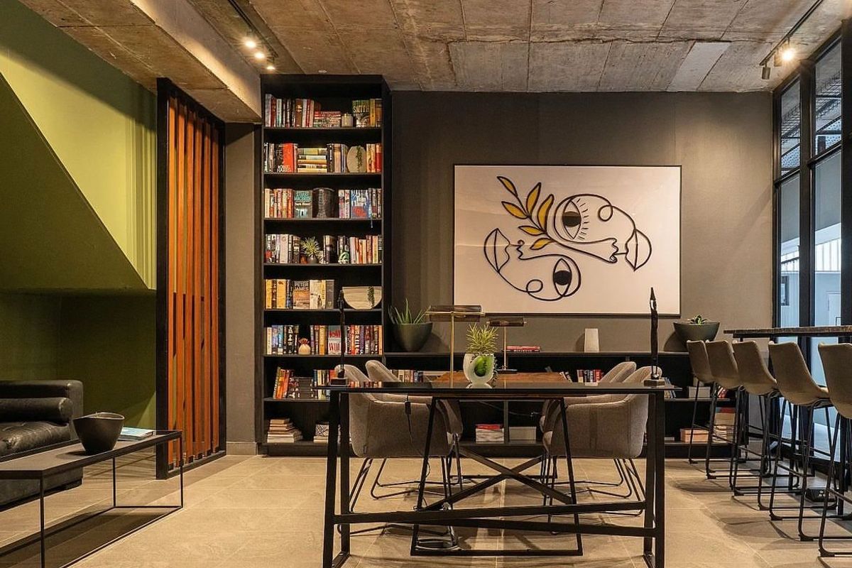 Modern living area featuring an exposed concrete ceiling, built-in floor-to-ceiling shelving, and large glass windows, creating a sophisticated and contemporary atmosphere.