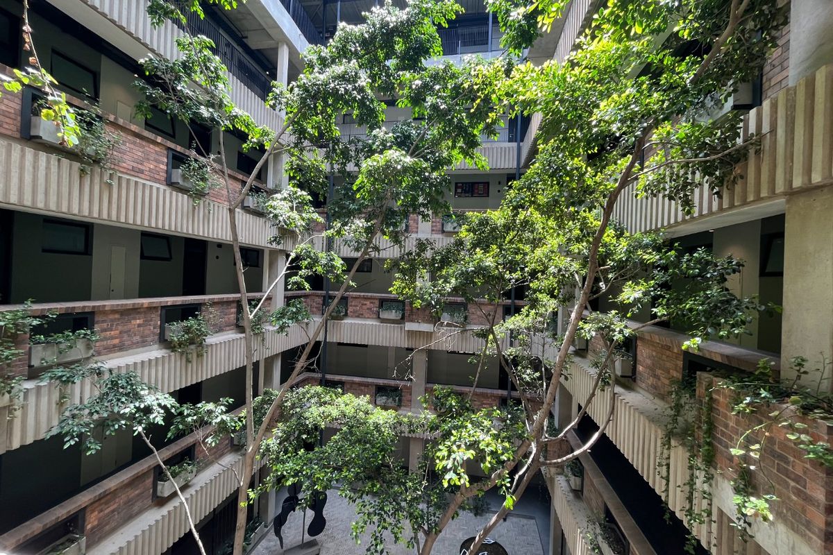 A multi-level apartment complex featuring an open-air central atrium with mature trees, brick facade detailing, and tiered walkways.