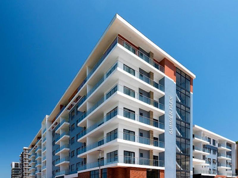 Modern multi-story apartment complex featuring contemporary architectural design, glass-fronted balconies, and a prominent corner facade with brick and painted finish detailing.