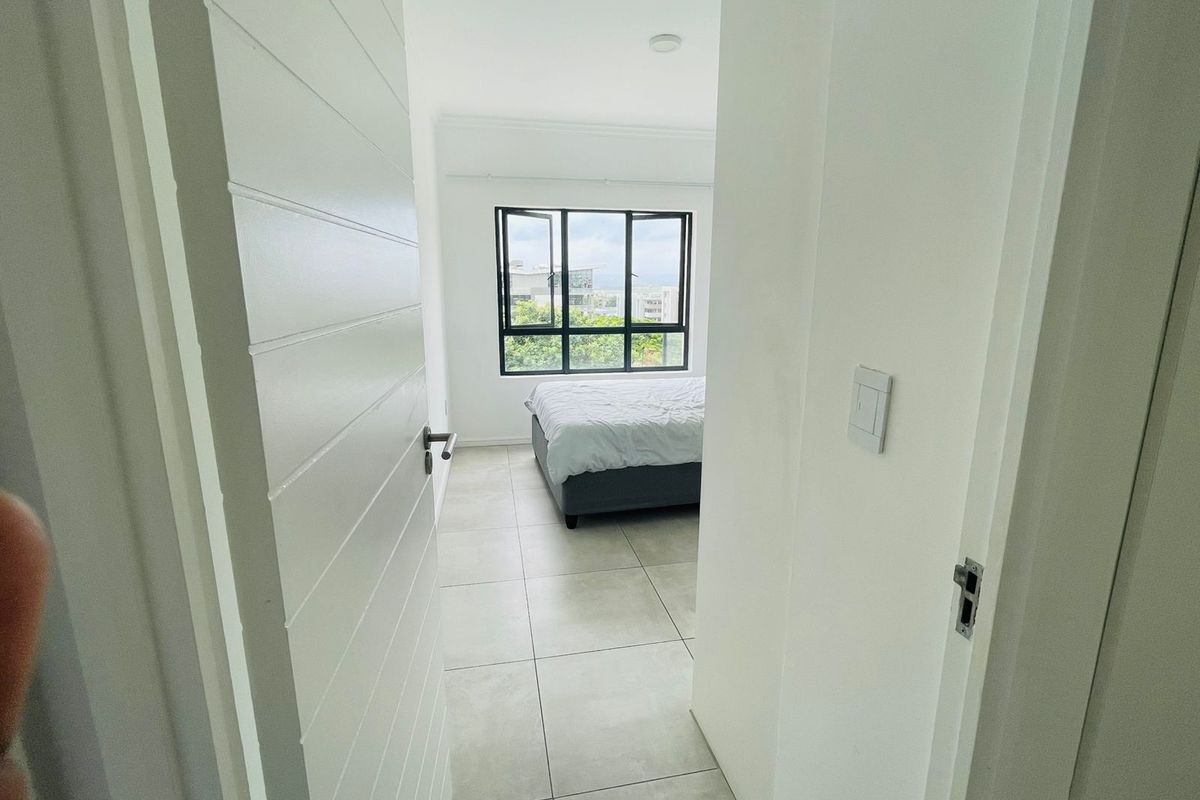 A bright bedroom featuring large windows with exterior views, neutral tiled flooring, and modern white interior doors.