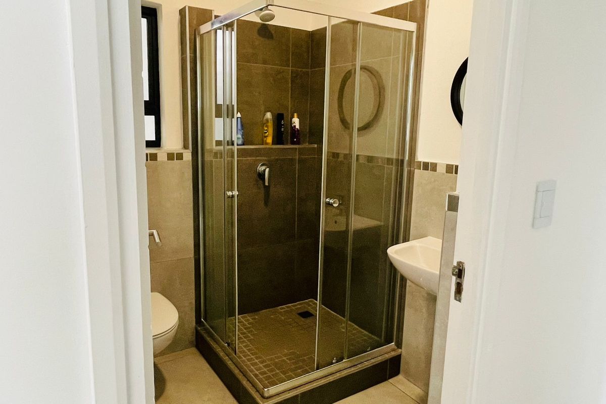 A compact bathroom featuring a glass-enclosed shower with tiled walls, a wall-mounted basin, and a toilet.