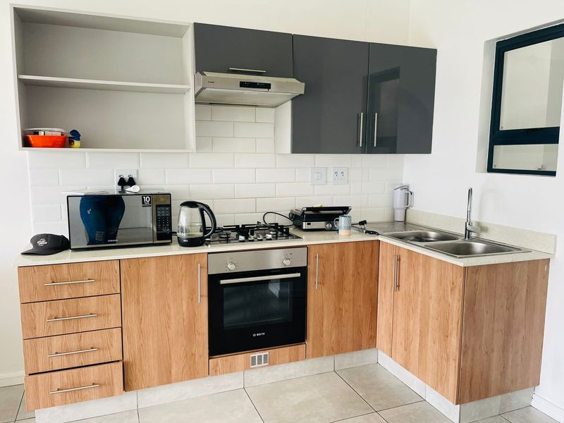 Modern kitchen featuring wood-look cabinetry, contrasting grey upper cabinets, subway tile backsplash, built-in oven, gas hob, extractor fan, and a double stainless steel sink.