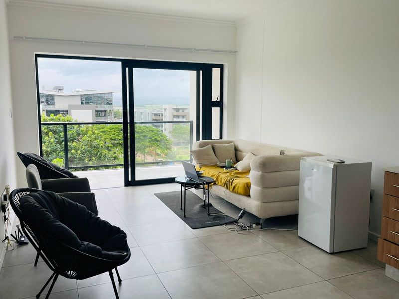 Open plan living area featuring large sliding glass doors leading to a balcony with scenic views and modern tiled flooring.