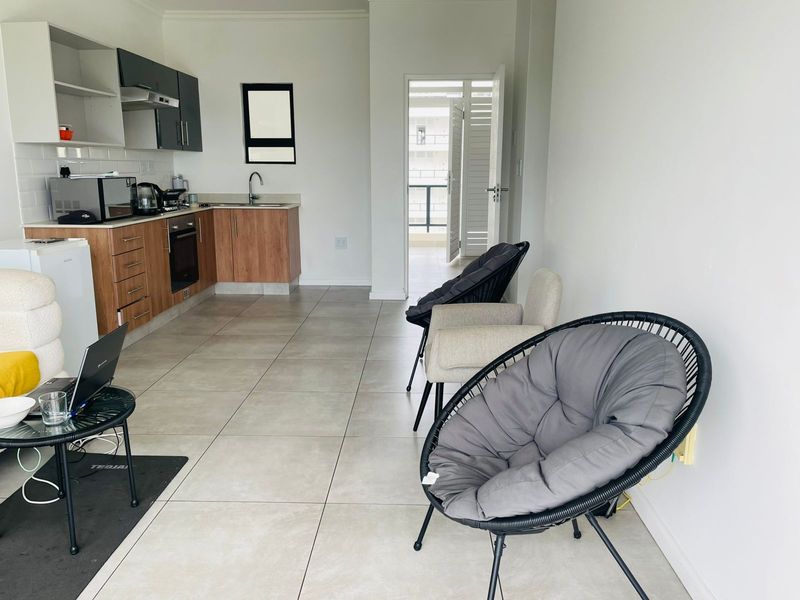 Open-plan living area featuring a modern kitchen with wood-finish cabinetry, tiled flooring, and direct access to a balcony.