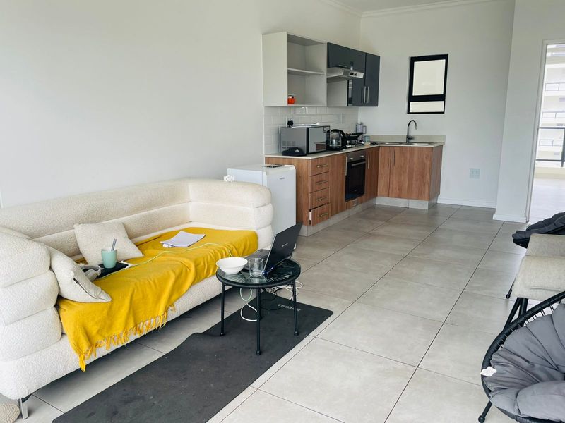 Open-plan living area featuring a compact kitchen with wood-finish cabinetry, integrated oven, hob, and extractor fan, leading to a tiled living space.