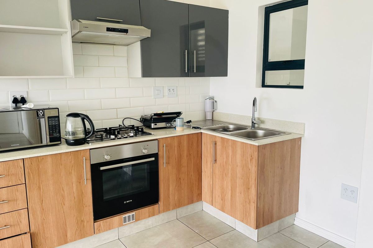 Modern kitchen featuring wood-finish cabinetry, stone countertops, subway tile backsplash, built-in oven, gas hob, and stainless steel double sink.