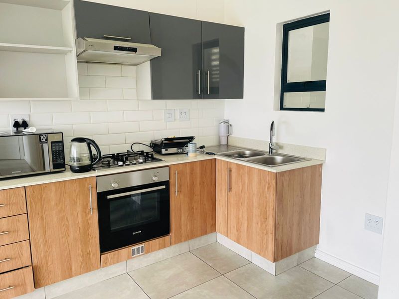 Modern kitchen featuring wood-finish cabinetry, stone countertops, subway tile backsplash, built-in oven, gas hob, and stainless steel double sink.