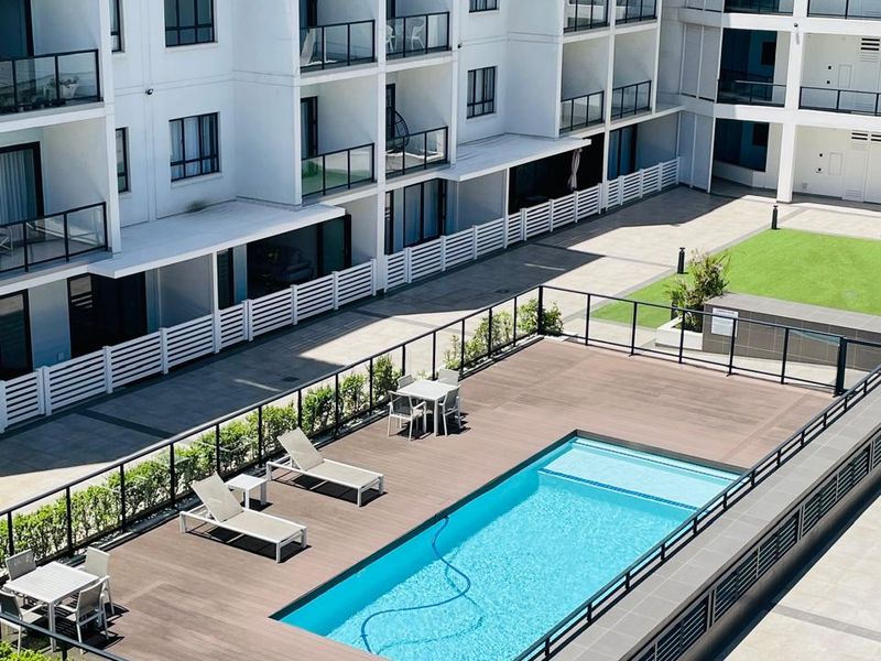 An elevated view of a modern apartment complex featuring a communal swimming pool with a timber deck and landscaped garden areas.
