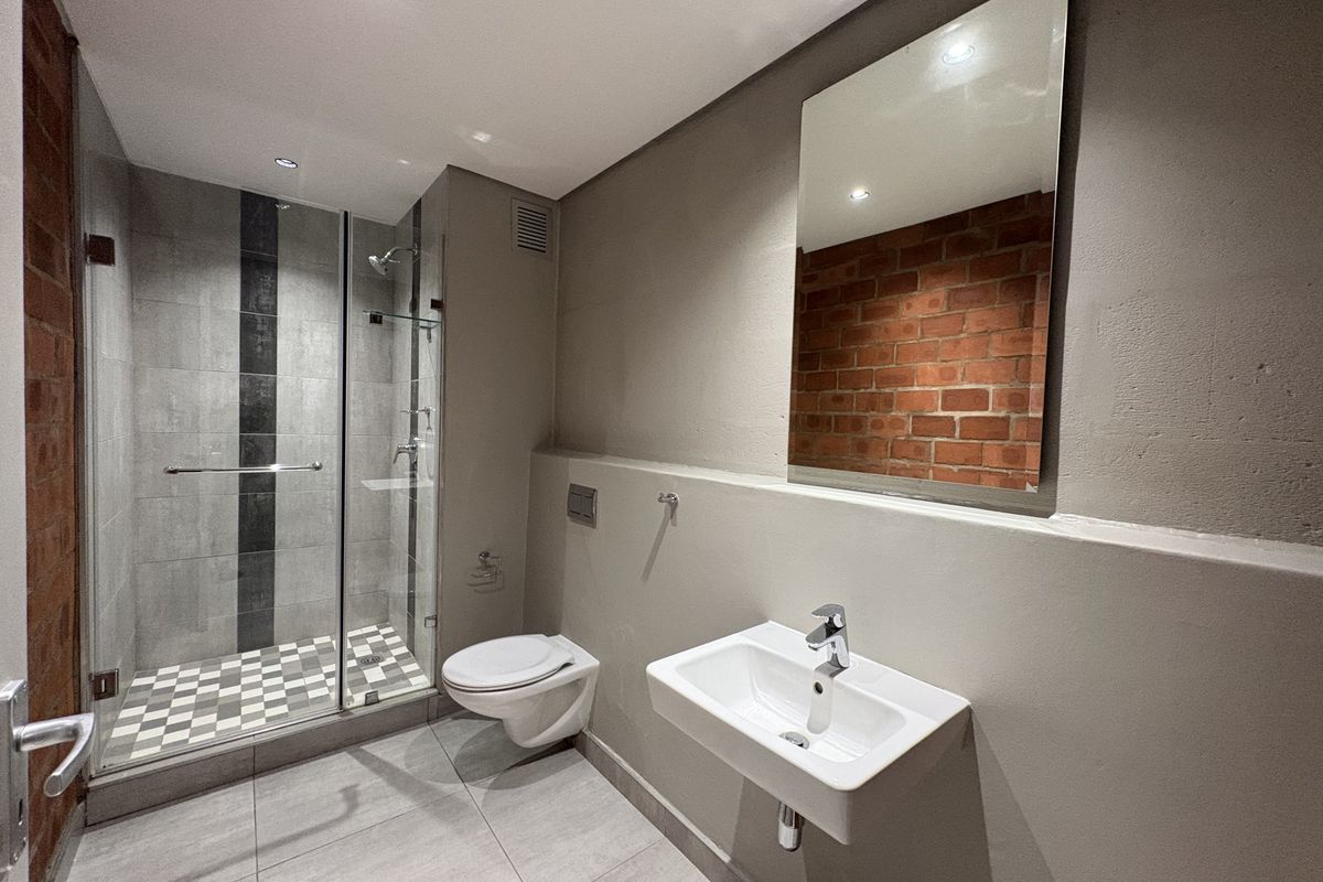 Modern bathroom featuring a glass-enclosed shower, wall-mounted toilet, floating vanity basin, and a stylish exposed brick feature wall.