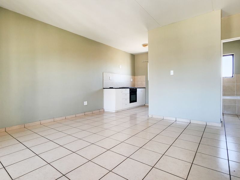 An open-plan living area featuring tiled flooring and a compact kitchen with built-in cabinetry and oven, leading to an adjacent bathroom.