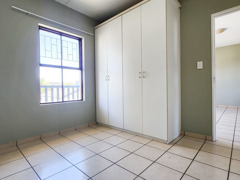 An empty bedroom featuring tiled flooring, a built-in wardrobe, and a window with security bars, offering a clean and functional space.