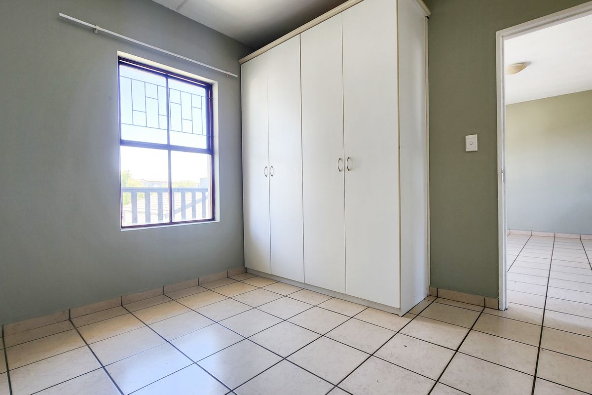 An empty bedroom featuring tiled flooring, a built-in wardrobe, and a window with security bars, offering a clean and functional space.