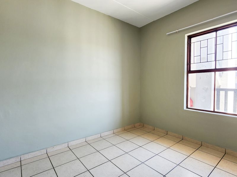 An empty bedroom featuring neutral wall paint, ceramic floor tiles, and a window fitted with security bars and a curtain rail.