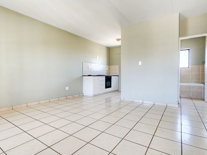 An open-plan living area featuring tiled flooring and a compact kitchen with built-in cabinetry, oven, and hob, leading to an adjacent bathroom.