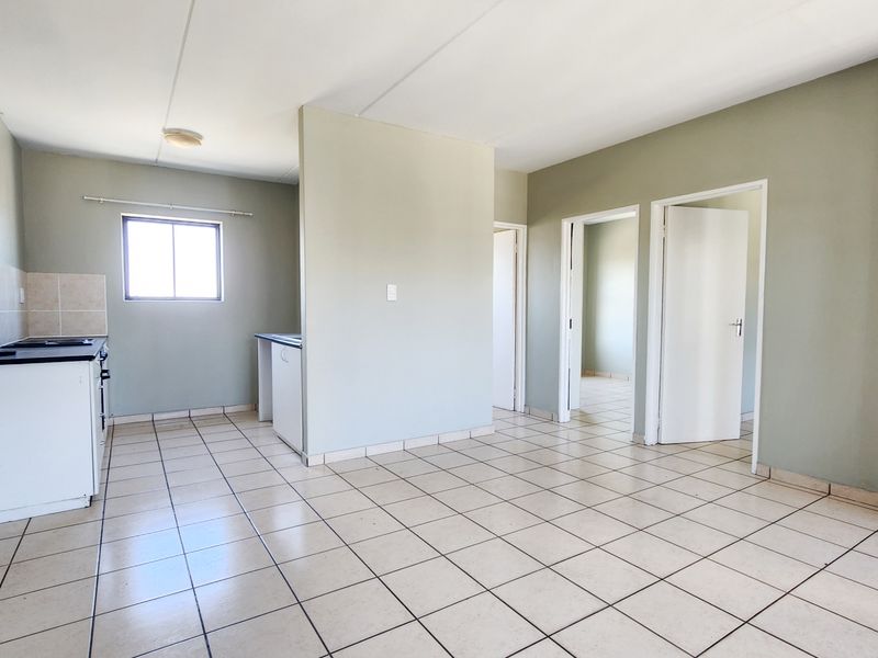 An open-plan living and kitchen area featuring tiled flooring, neutral walls, and built-in kitchen cabinetry with a stove.