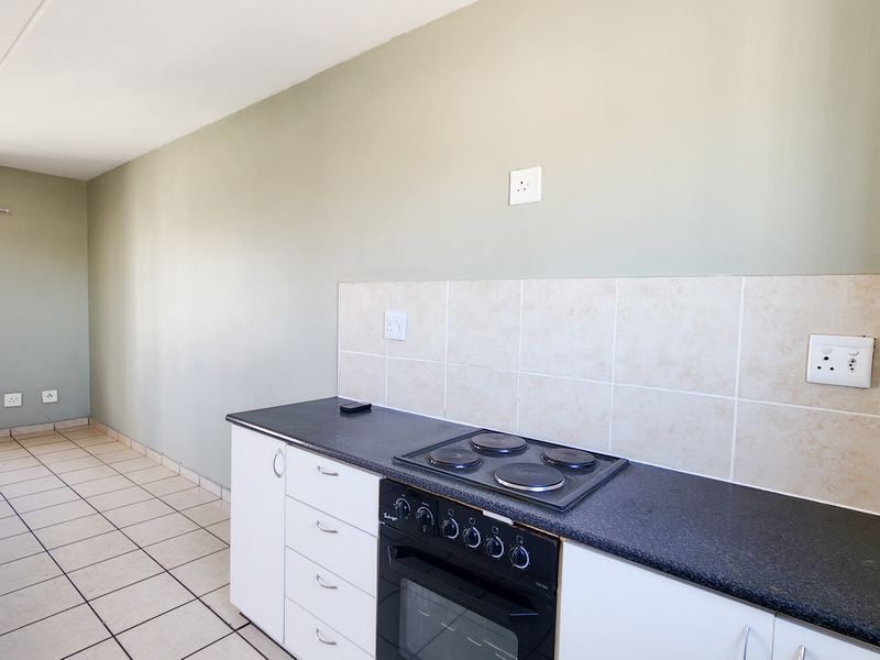 A functional kitchen area featuring white cabinetry, a built-in oven with electric hob, tiled splashback, and neutral tiled flooring.