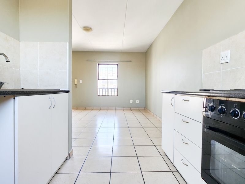 An open-plan kitchen and living area featuring tiled flooring, built-in cabinetry, and a functional oven, offering a clean, blank canvas for personalization.