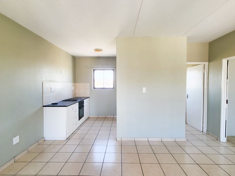 An open-plan living and kitchen area featuring tiled flooring, neutral walls, and a functional built-in kitchen unit with an integrated oven and hob.