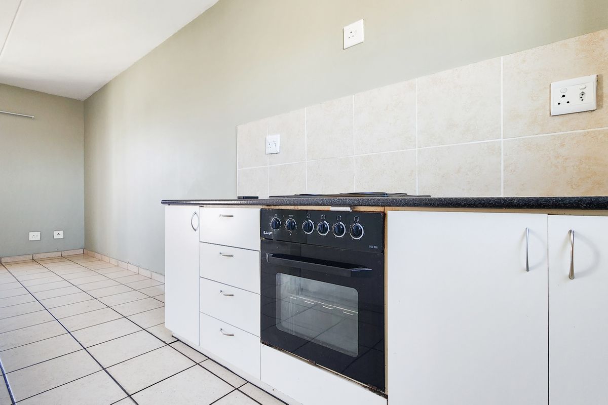 A functional kitchen area featuring white cabinetry, a built-in oven with hob, tiled splashback, and neutral tiled flooring in an open-plan layout.