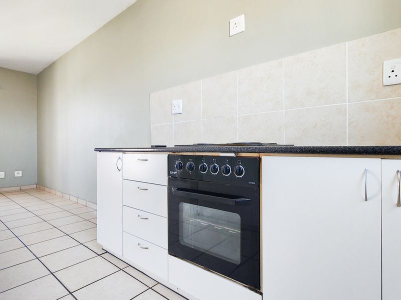 A functional kitchen area featuring white cabinetry, a built-in oven with hob, tiled splashback, and neutral tiled flooring in an open-plan layout.