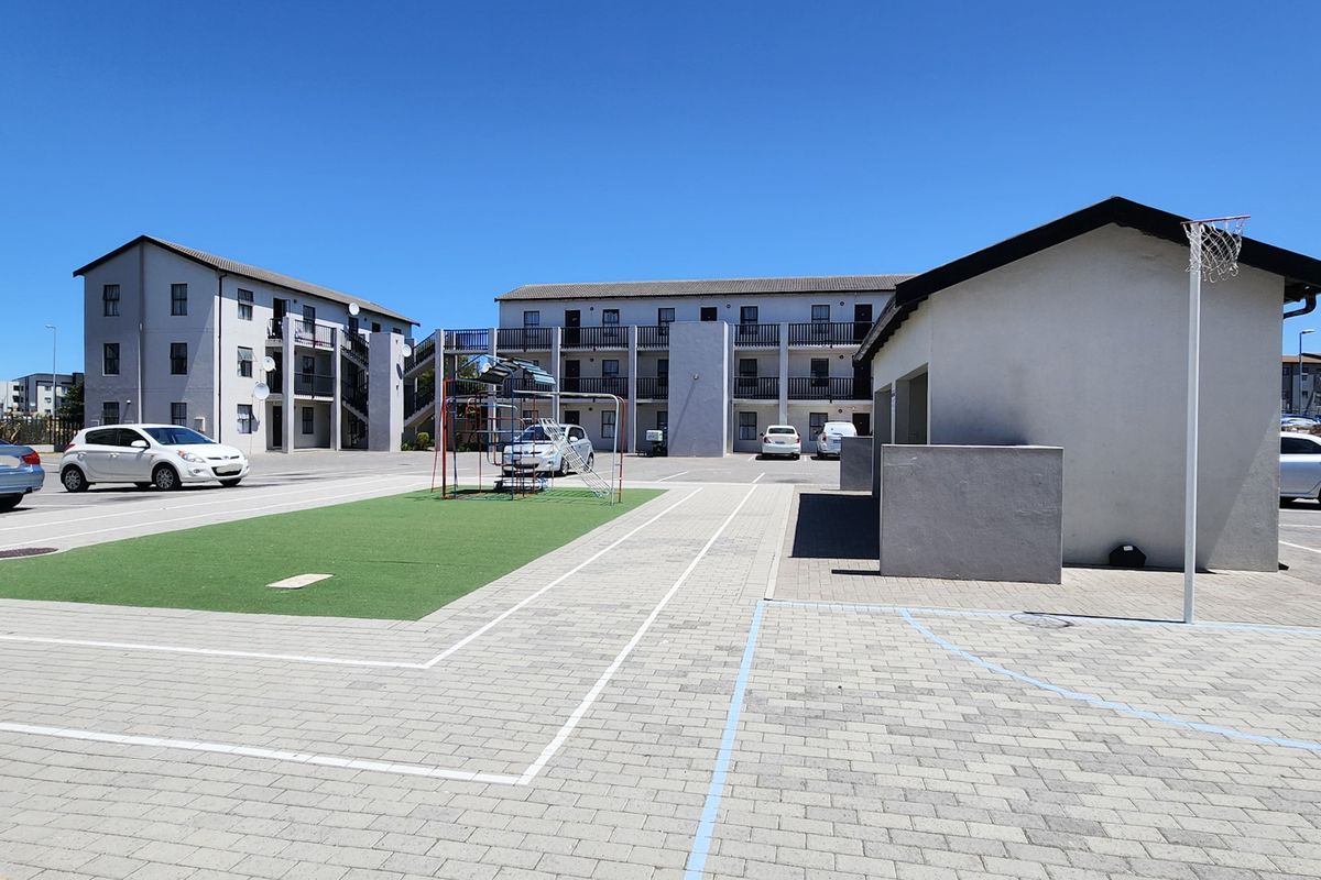 Exterior view of a residential apartment complex featuring a paved courtyard, artificial turf area, and recreational facilities.