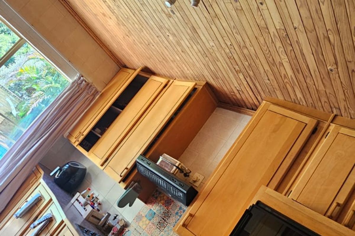 A functional kitchen featuring timber cabinetry, a patterned tile backsplash, and a built-in oven, set under a natural wood-paneled ceiling.