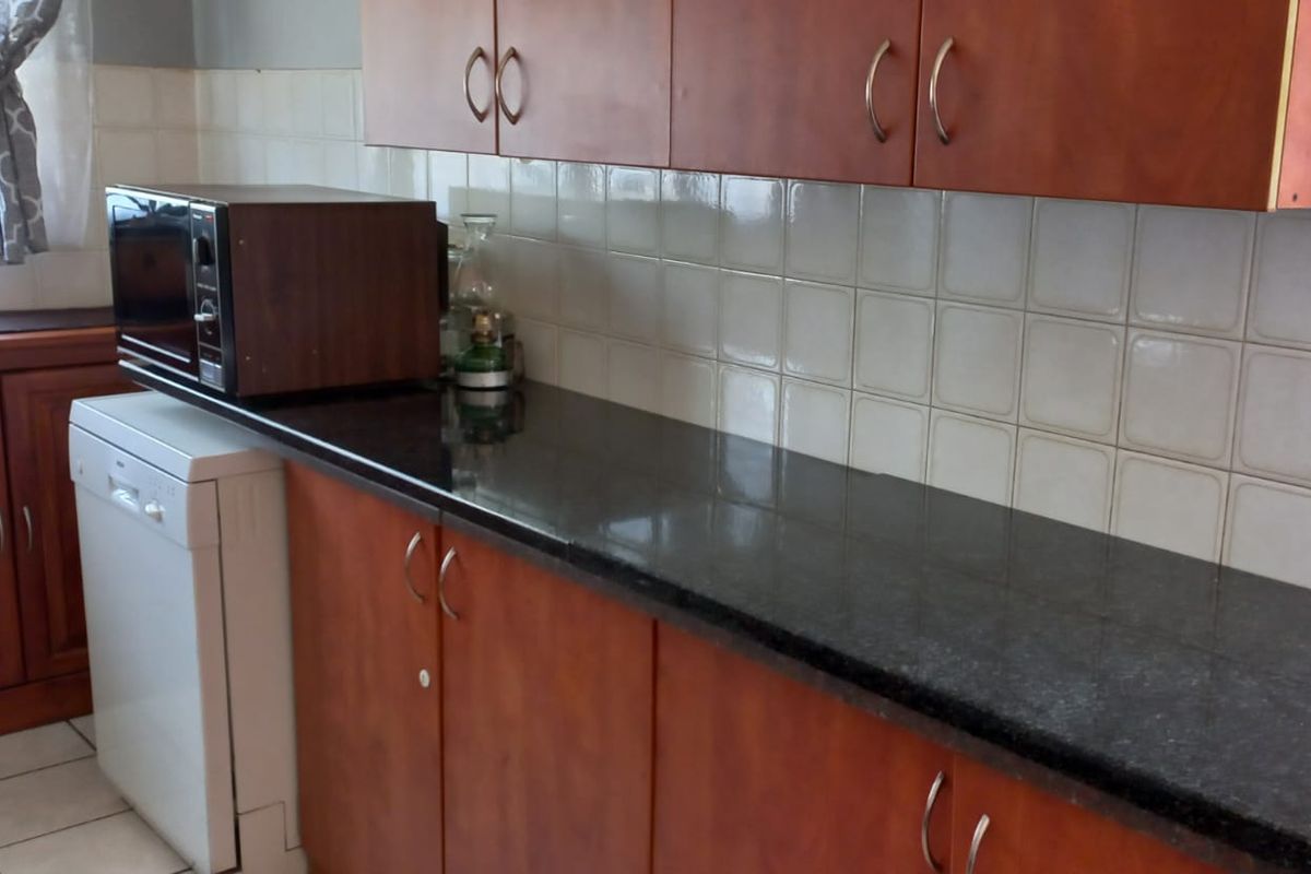 A functional kitchen area featuring dark stone countertops, wooden cabinetry, and tiled splashbacks, providing a practical workspace for daily meal preparation.