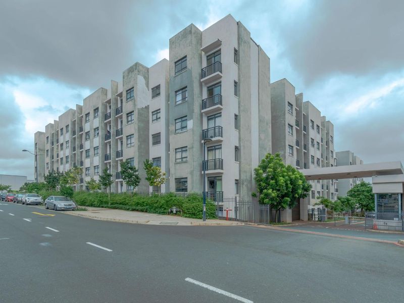 A street-level view of a modern multi-story apartment complex featuring balconies and a secure gated entrance.
