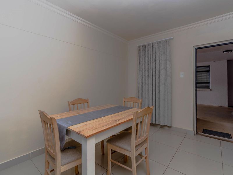 A simple dining area featuring neutral tiled flooring, crown molding, and a doorway leading to an adjacent room.