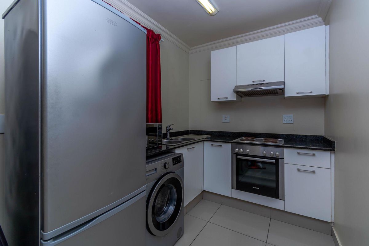 Compact kitchen featuring white cabinetry, granite countertops, built-in oven, hob, and extractor fan, with integrated space for laundry appliances.