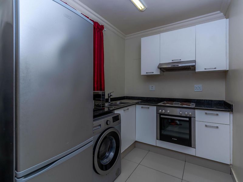Compact kitchen featuring white cabinetry, granite countertops, built-in oven, hob, and extractor fan, with integrated space for laundry appliances.