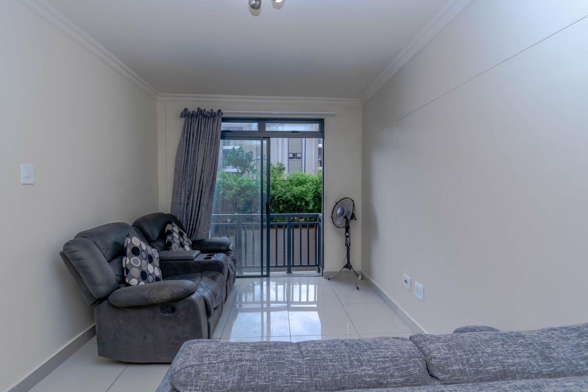 A bright living room featuring large sliding glass doors that open onto a balcony, complemented by neutral tiled flooring and crown molding.