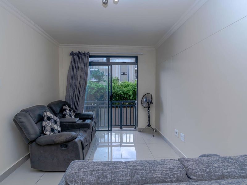 A bright living room featuring large sliding glass doors that open onto a balcony, complemented by neutral tiled flooring and crown molding.