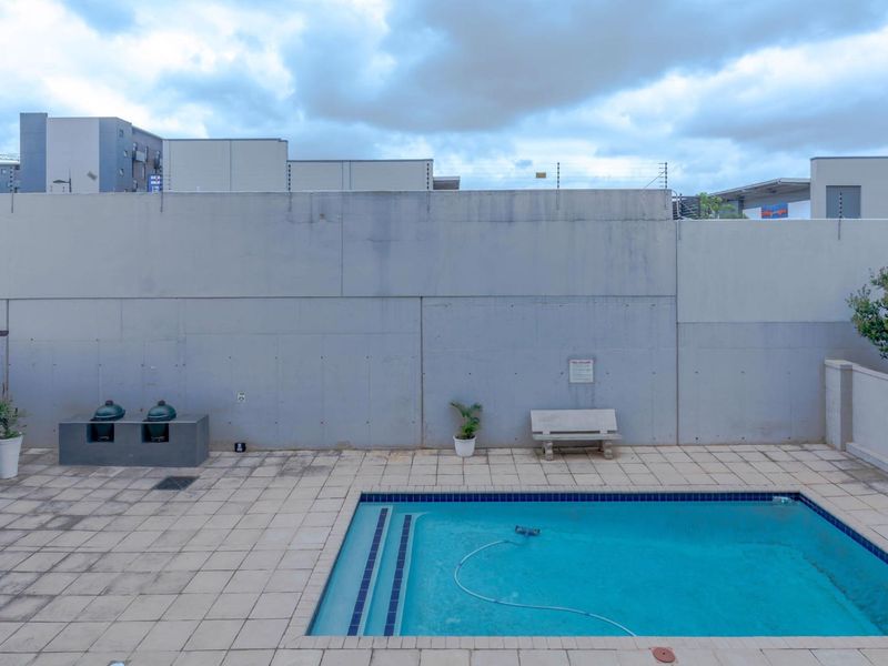 Outdoor pool area featuring a swimming pool with tiled surround, built-in concrete bench, and high boundary wall.