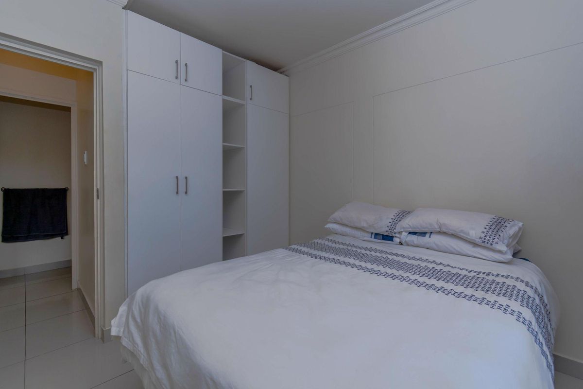 A well-maintained bedroom featuring built-in white cabinetry with integrated shelving and tiled flooring, providing a clean and functional living space.