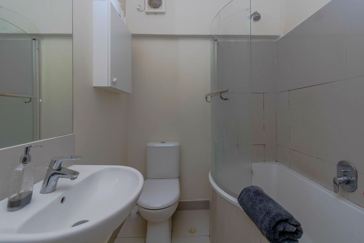 Compact bathroom featuring a white pedestal sink, toilet, and a shower-over-bath combination with a curved glass screen.