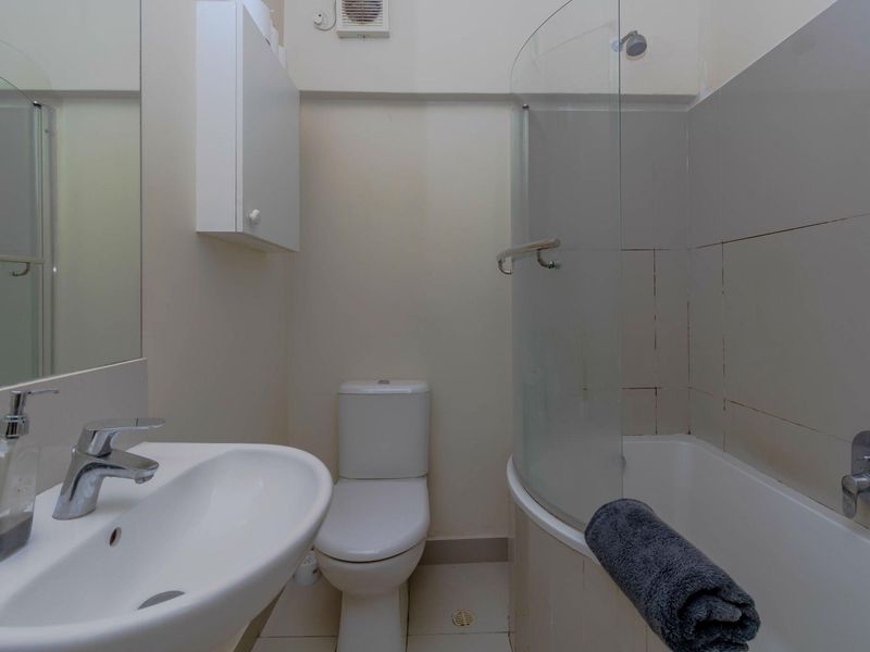 Compact bathroom featuring a white pedestal sink, toilet, and a shower-over-bath combination with a curved glass screen.