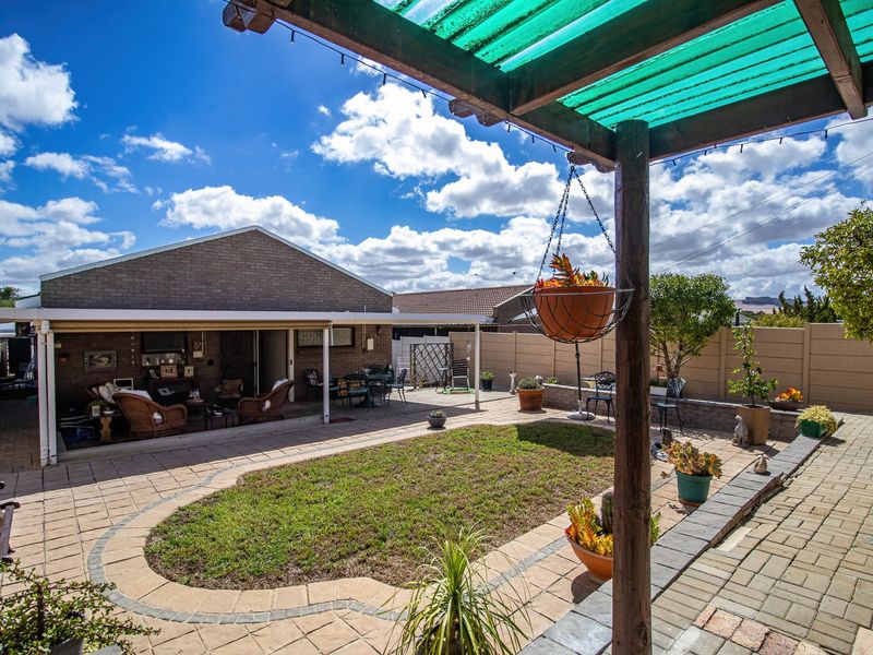 A spacious rear courtyard featuring a covered patio area, paved flooring, a central lawn, and a timber pergola structure.