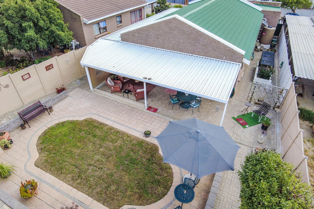 Aerial view of a rear garden featuring a paved patio area with a covered roof structure, a small lawn, and perimeter boundary walls.