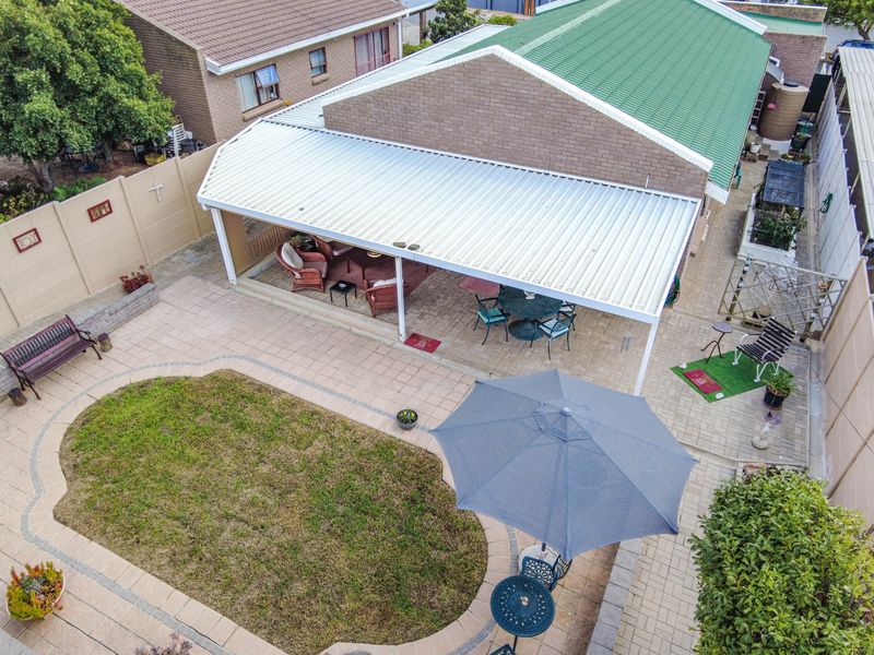 Aerial view of a rear garden featuring a paved patio area with a covered roof structure, a small lawn, and perimeter boundary walls.